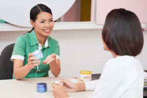 Pretty Vietnamese beautician demonstrating new cream to young woman