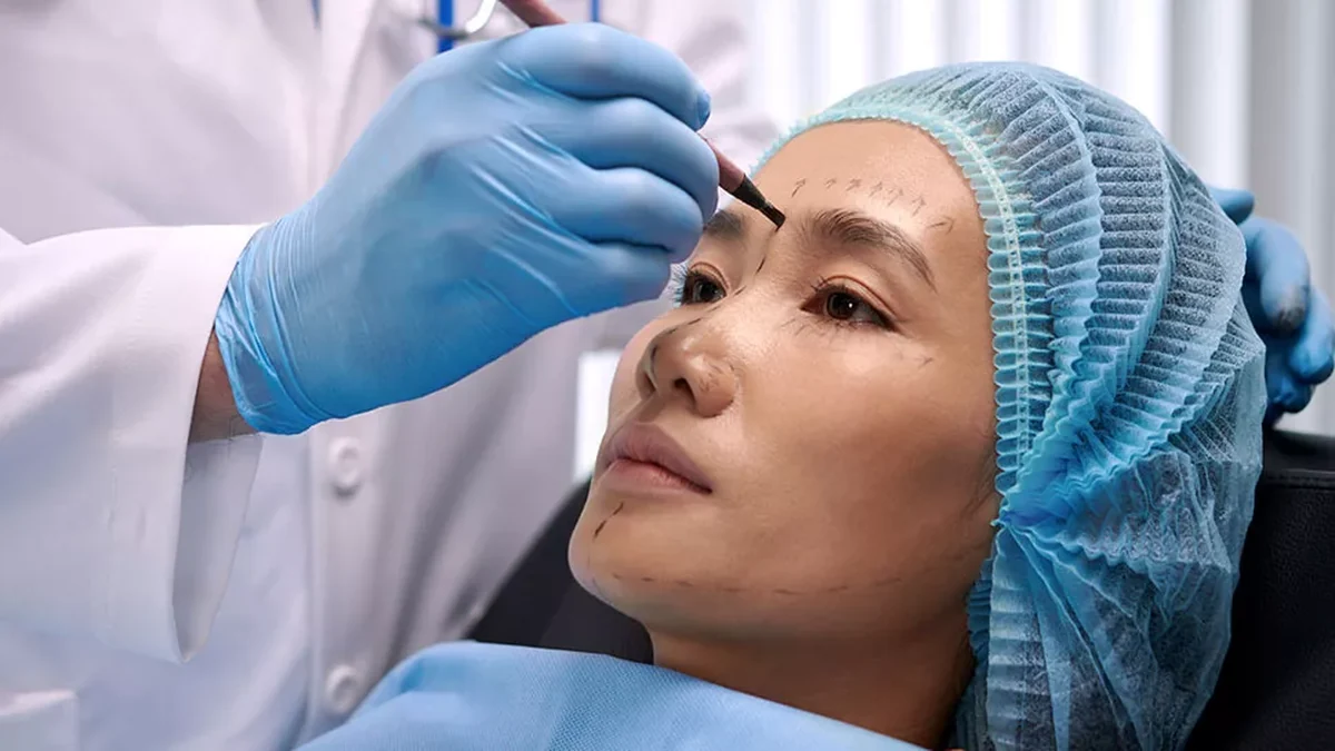 Doctor marking the face for facelift assessment, mapping the brow, mid-face and jawline before treatment planning